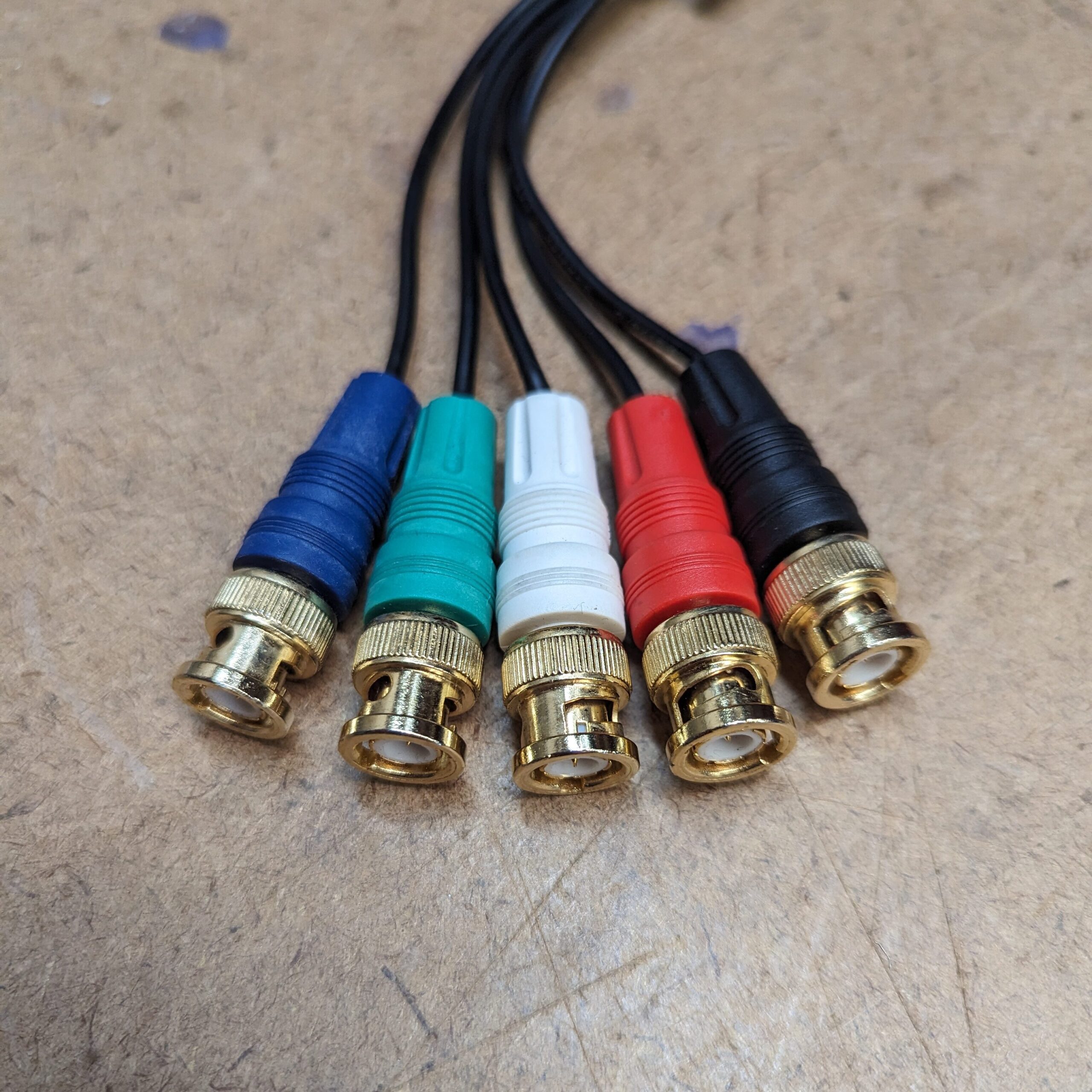 "A close-up of an RGBHV cable, showcasing its five BNC connectors in a row, each with a colored plastic housing (blue, green, white, red, black), used for carrying video signals; red, green, blue and vertical and horizontal sync.