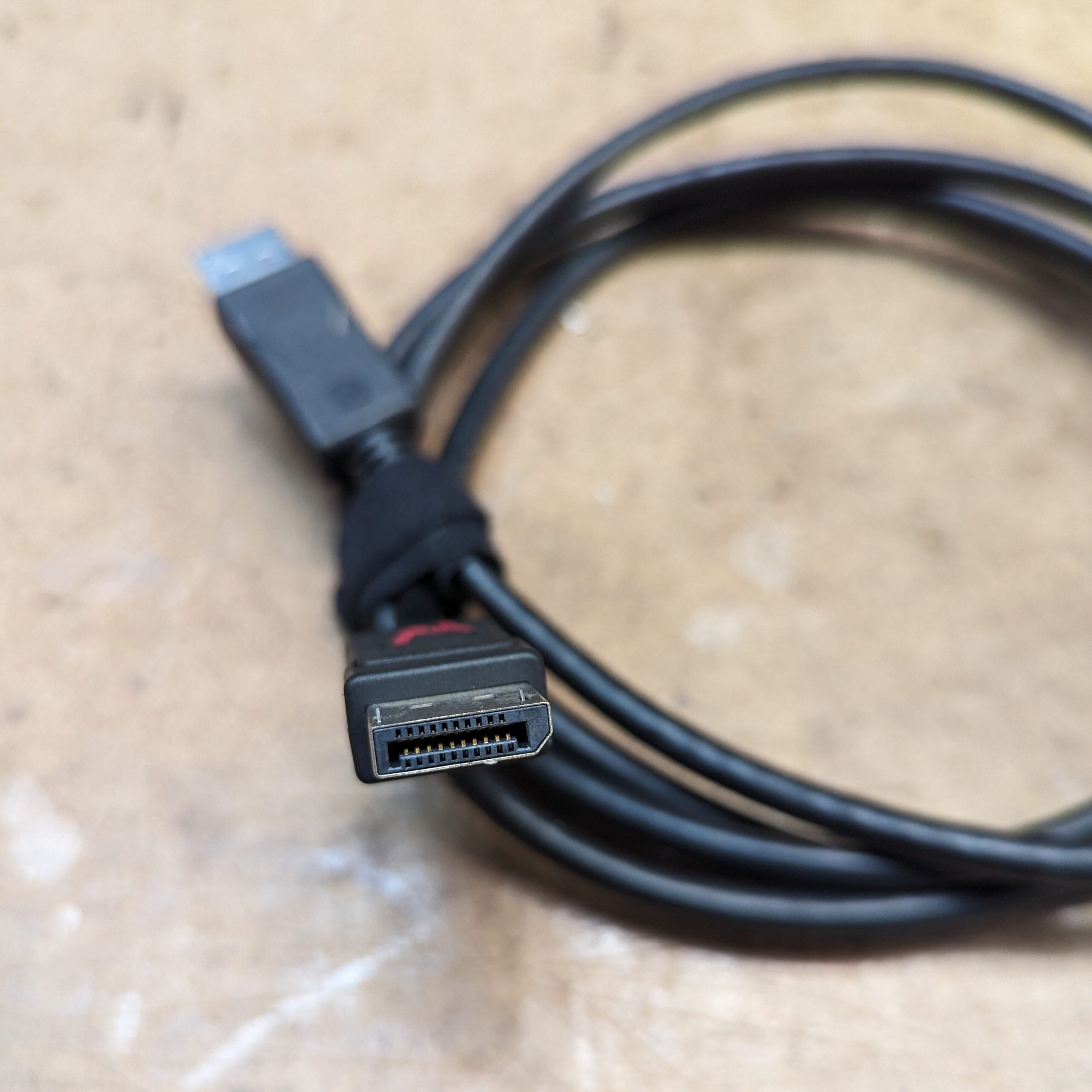 A black DisplayPort cable with the metal connector, showing the many pins, visible in the foreground. The cable is looped in the background.